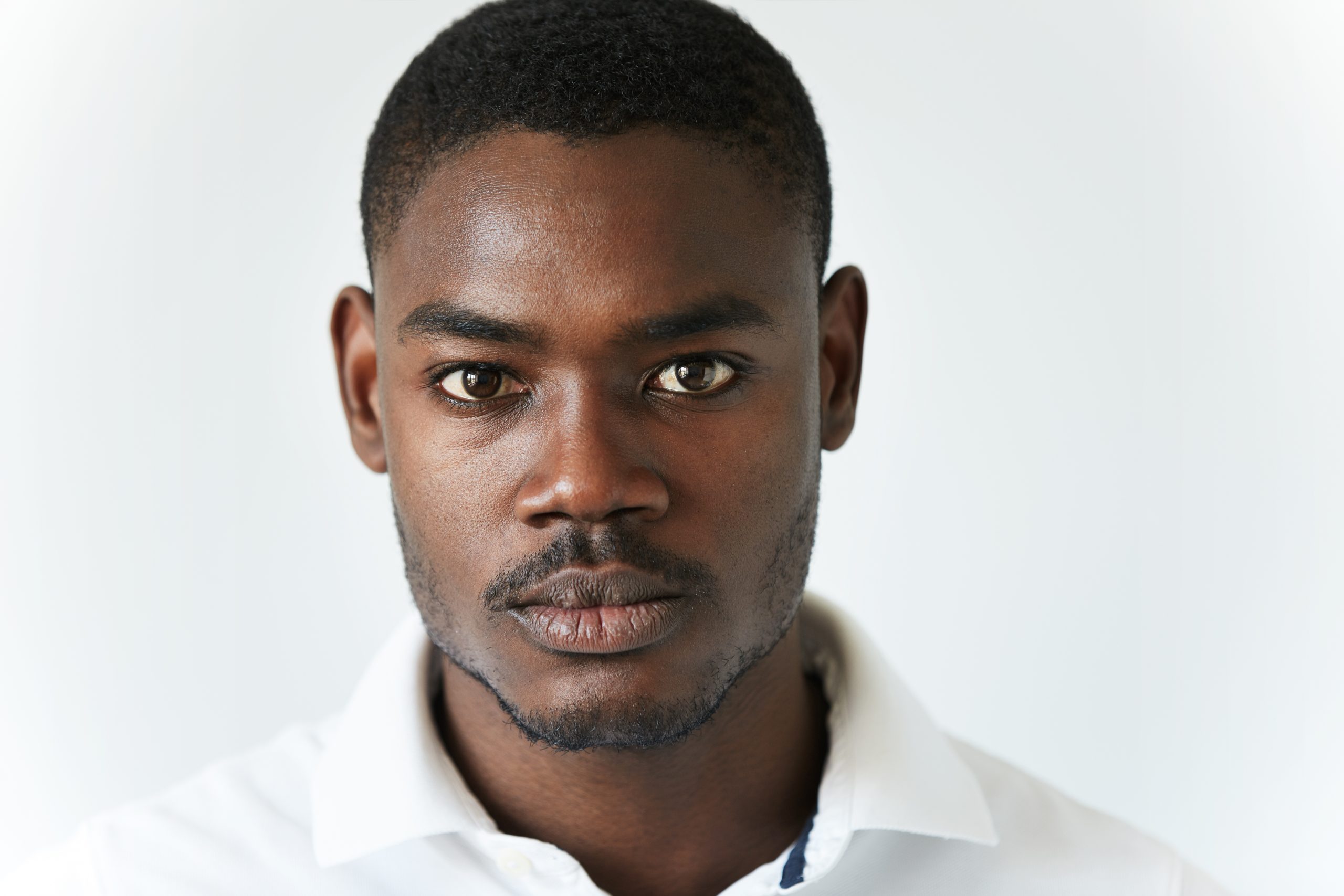 Highly-detailed close up portrait of handsome young African American man wearing stylish polo shirt, looking at the camera with serious thoughtful expression. Human face expression and emotions