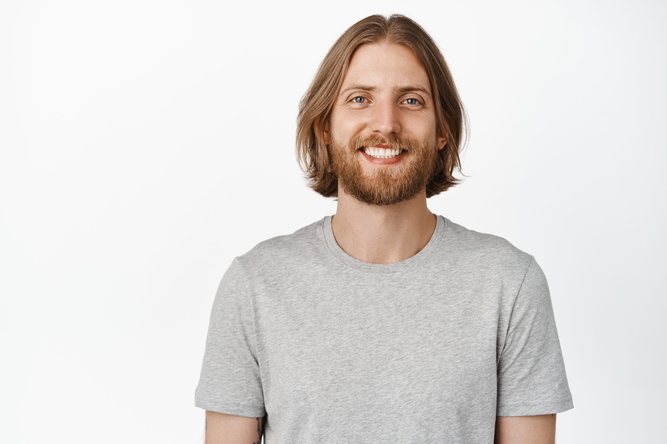 Happy smiling man with blond hair and beard, looking at camera, standing in grey t-shirt, isolated on white background